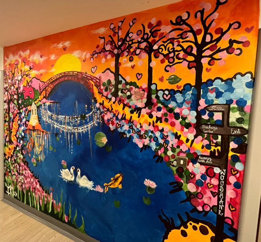 Colorful mural depicting a vibrant landscape with trees, a river, and a bridge adorned with various whimsical elements like flowers and abstract designs.