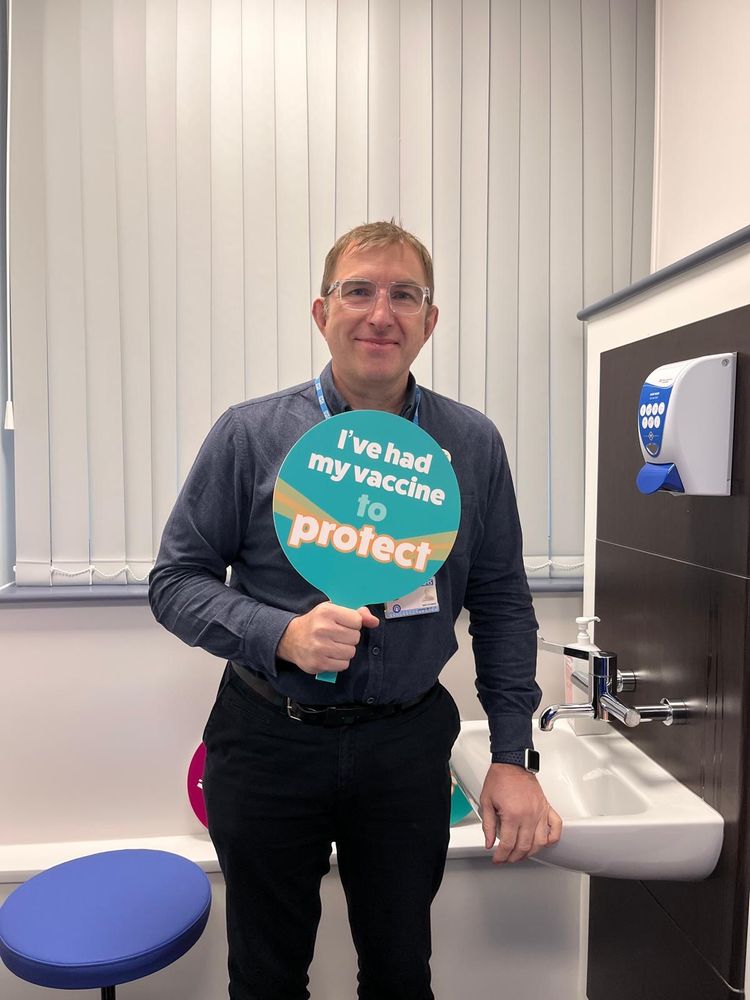 A healthcare professional holding up a green sign which says 'I've had my vaccine to protect'