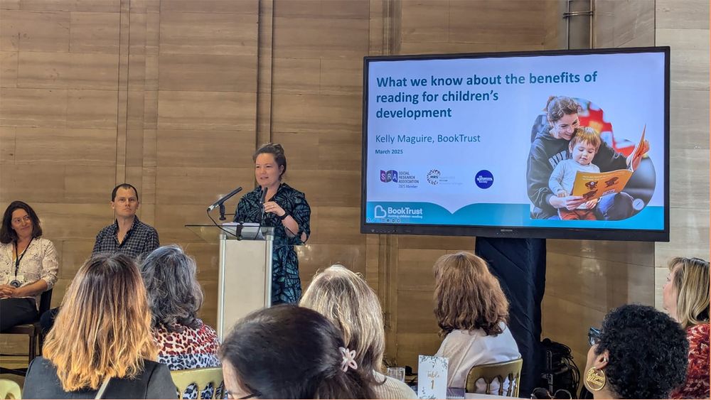 Kelly Maguire speaking to delegates at the Early Years Reading Conference; a screen in the background reads "What we know about the benefits of reading for children's development"