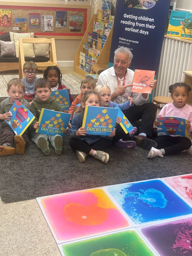 Frank holding the Reading Rights report while a group of children sit on the floor of the nursery holding books