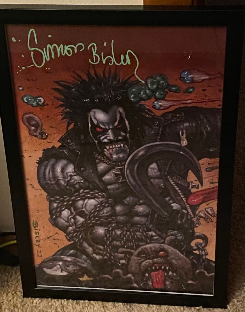 A print of Lobo and Dawg by Simon Bisley. Lobo has his trademark hook and chain on his right arm, and is punching off to the left with his… left. Gore and brain matter fly in from his victim. The background fades from dark to lighter orange as one scans from top to bottom. 

A green signature from Bisley is in the top left corner. 