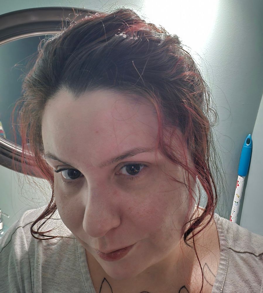 a selfie of me. my hair is mostly tied back, but with texture on the top and waves beside my face. I have highlights that I've dyed red