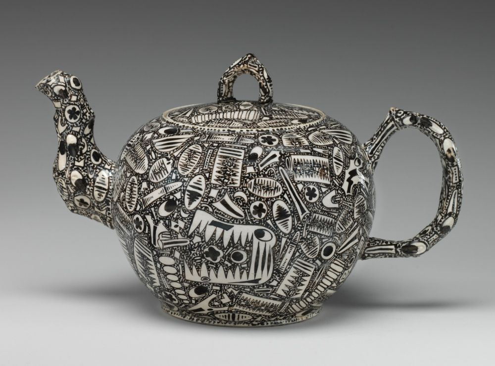 a black and white teapot decorated with abstract fossils and eyes, including one that looks like some sort of crocodile — overall, it looks like something hallucinogenic from the 1960s but is really from the 1760s