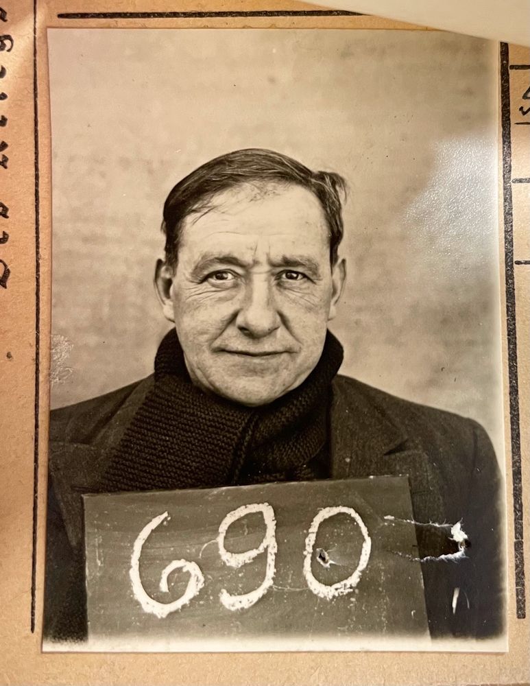 mugshot of a man in his 50s with dark hair, wearing a knit scarf, holding a slate with number 690 in chalk

from The National Archives (UK) WO 416