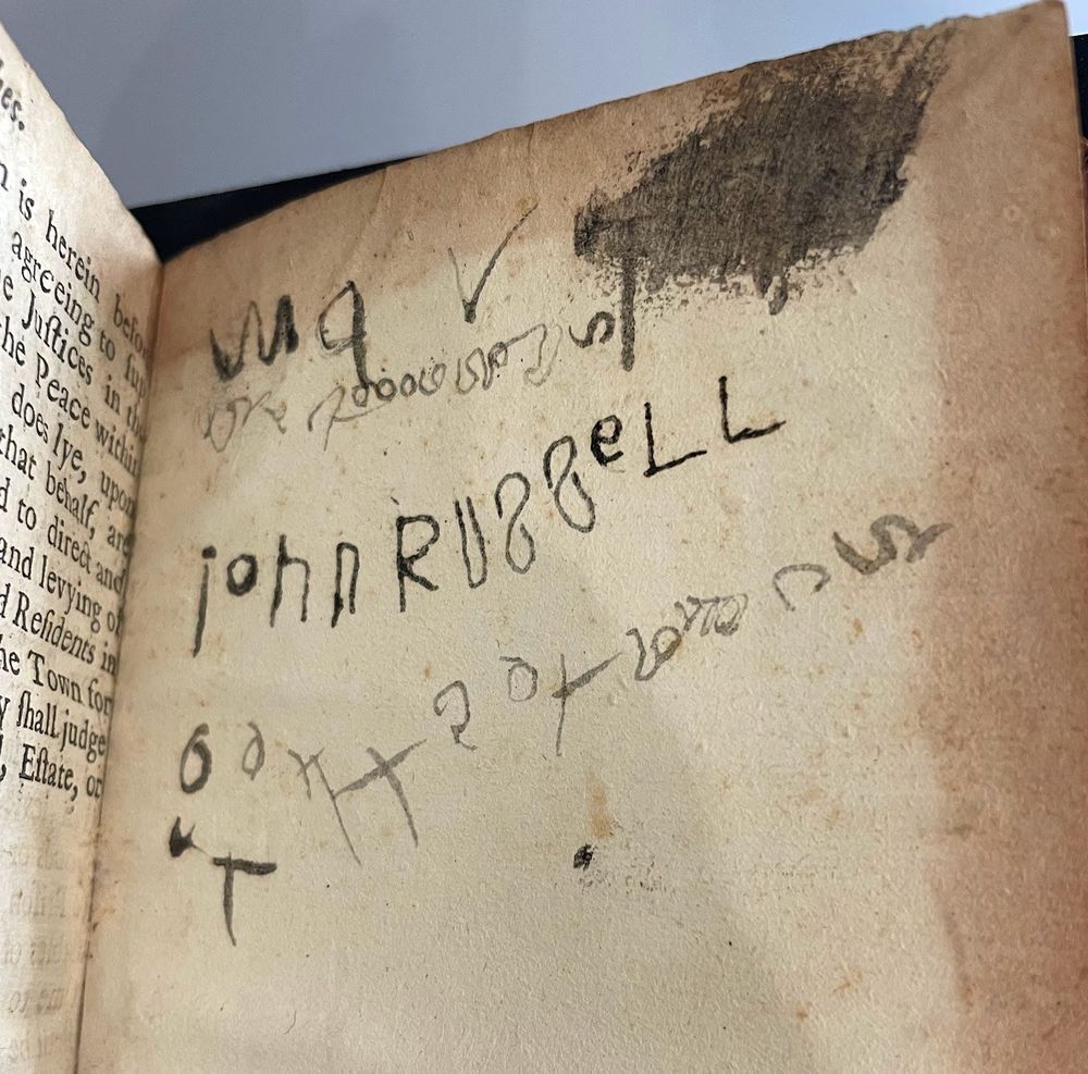 endpaper from an 18th-century book showing the name John Russell in a childish hand with the S backwards and blobby ink, along with other doodles and practice letters