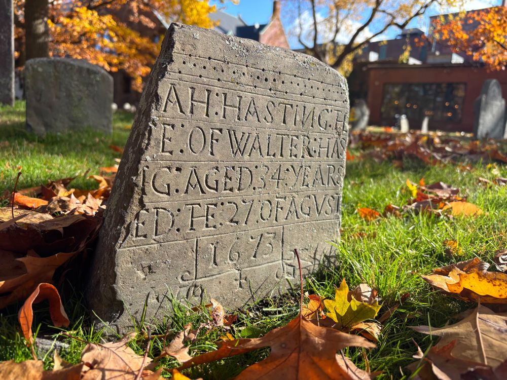a small, broken gravestone with capital letters carved under a design of dots. The inscription is partially broken off, but it would say "Sarah Hasting the wife of Walter Hasting aged 34 years died the 27 of Augst 1673