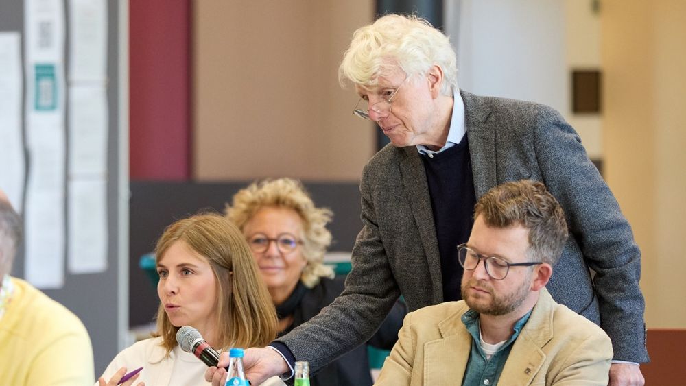Diskussionsszene beim Fachtag in Berlin: Eine junge Frau spricht ins Mikrofon, während ein älterer Mann das Mikro hält. Beate Müller-Gemmeke sitzt im Hintergrund und hört aufmerksam zu.