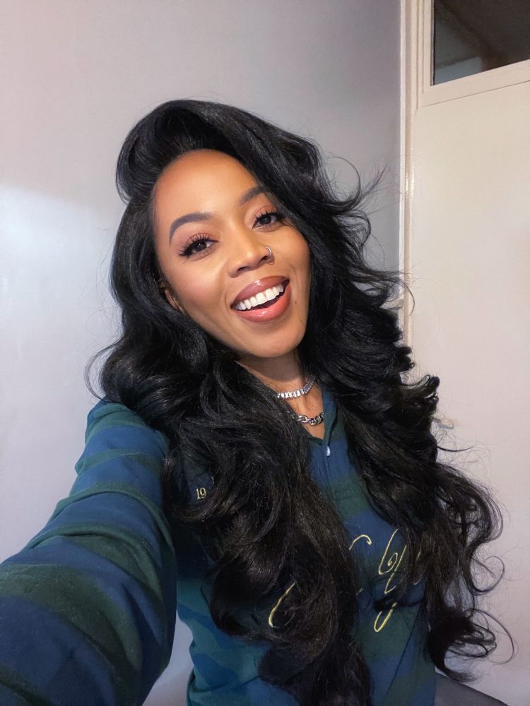 Smiling selfie 1. Long black loose curly hair & wearing dark green & navy striped long sleeve rugby shirt with gold “New York” text on the front 