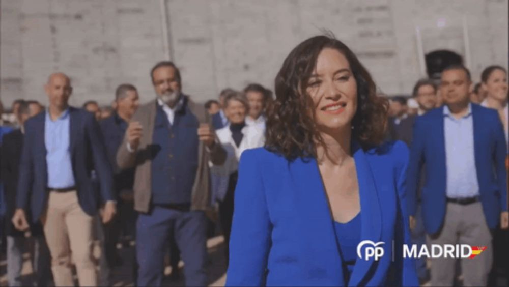 a woman in a blue jacket stands in front of a crowd with madrid written on the bottom right