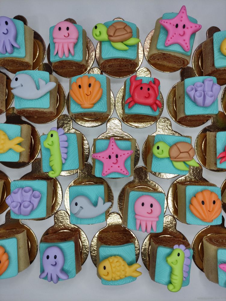 vários bolinhos de rolo em forminhas individuais douradas, com fundo azul claro e decoração de animais marinhos coloridos. 