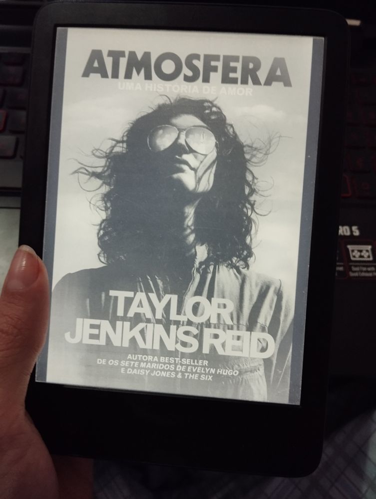 Foto da capa do livro Atmosfera, de Taylor Jenkins-Reid, com mulher usando óculos de sol, jaqueta de astronauta enquanto olha pro céu 
