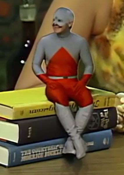 A bad cosplay of the DC comics character the Atom from the 1970s sitting on top of some books.