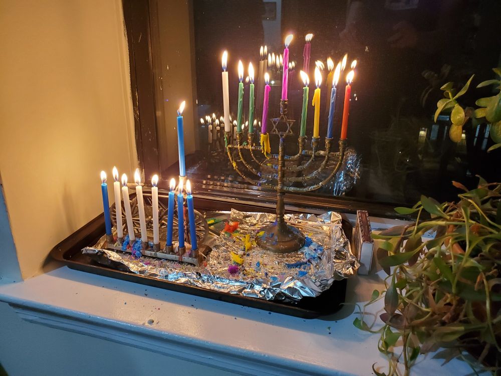 Two menorahs in a window with nine candles lit and burning.