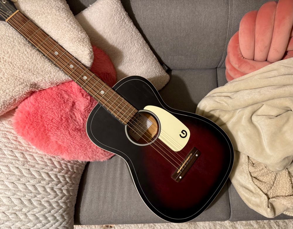 Foto einer kleinen Gretsch-Folkgitarre, die auf einem Sofa liegt.