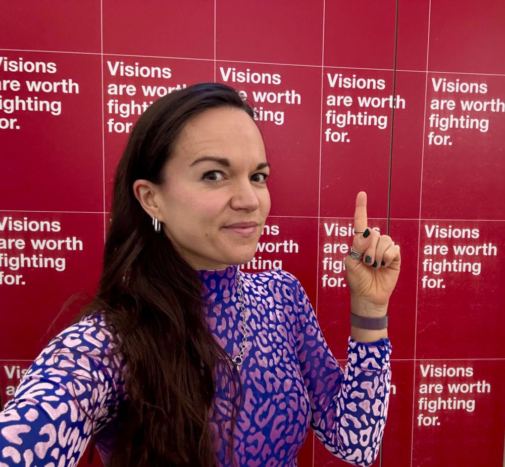 Ich vor einer Wand, auf der mehrere rote Poster hängen mit der Aufschrift „Visions are worth fighting for.“