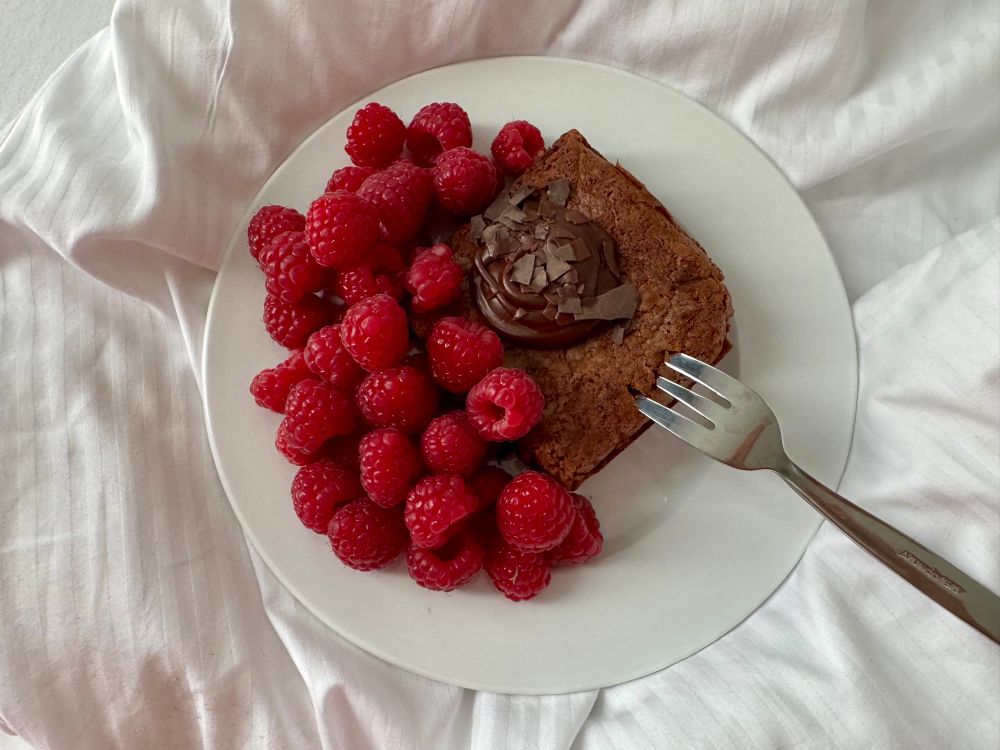 Ein Brownie mit Nussnougatcreme obendrauf und Himbeeren dazu
