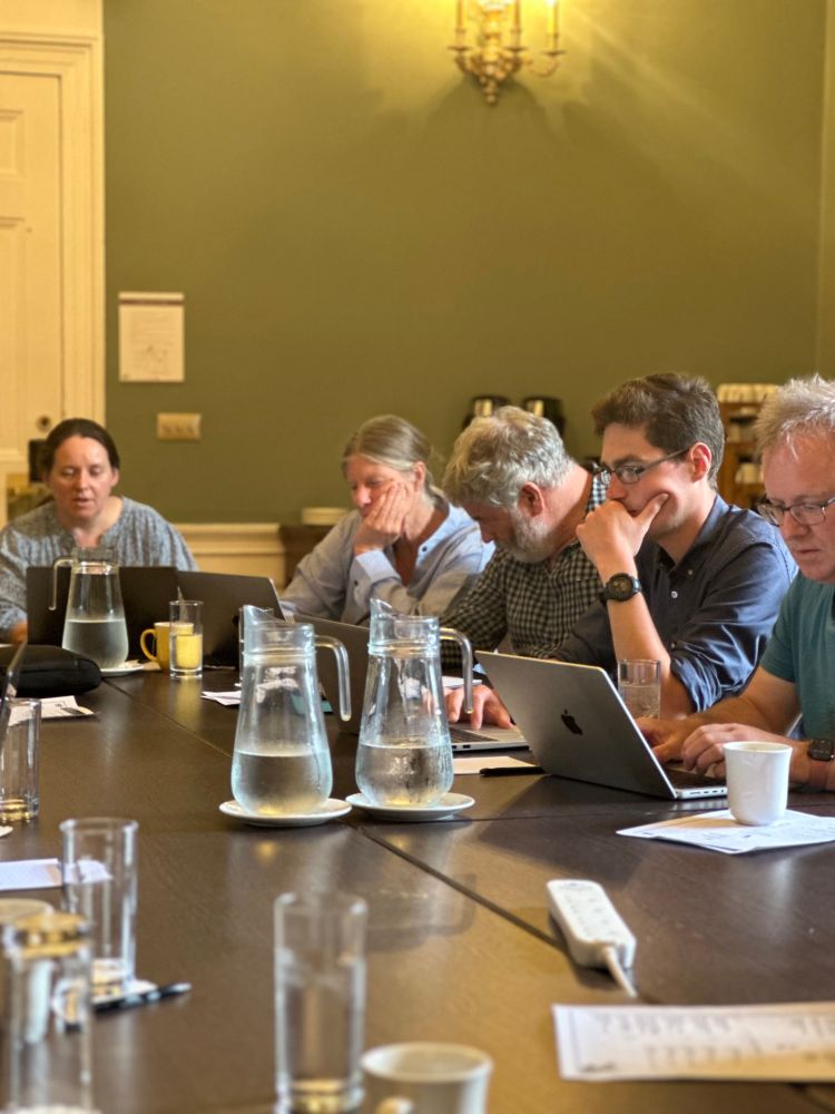 Researchers at a board room table use their computers during an interactive workshop session.