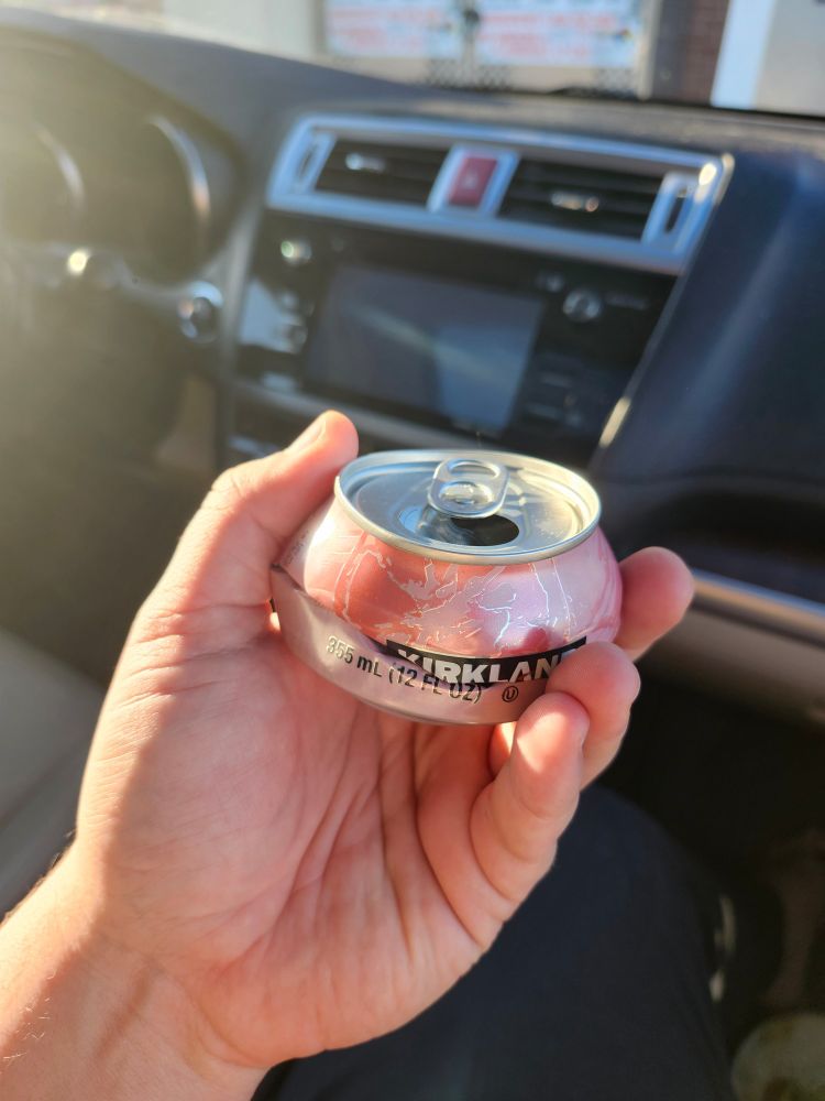 Hand holding a crushed soda can that is crushed from top down