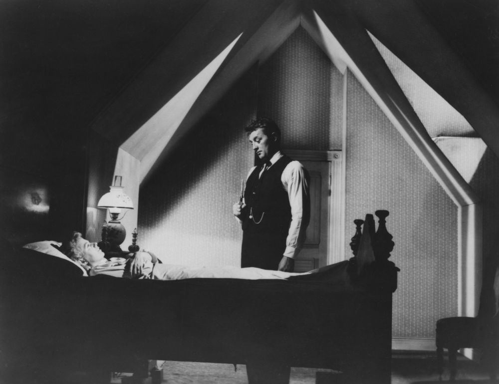Robert Mitchum standing over Shelley Winters in bed in the film THE NIGHT OF THE HUNTER (1955).