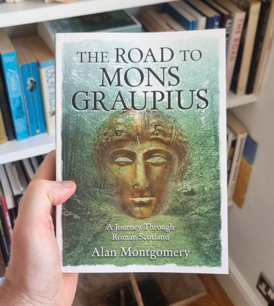 My hand holding a copy of my book, the Road to Mons Graupius