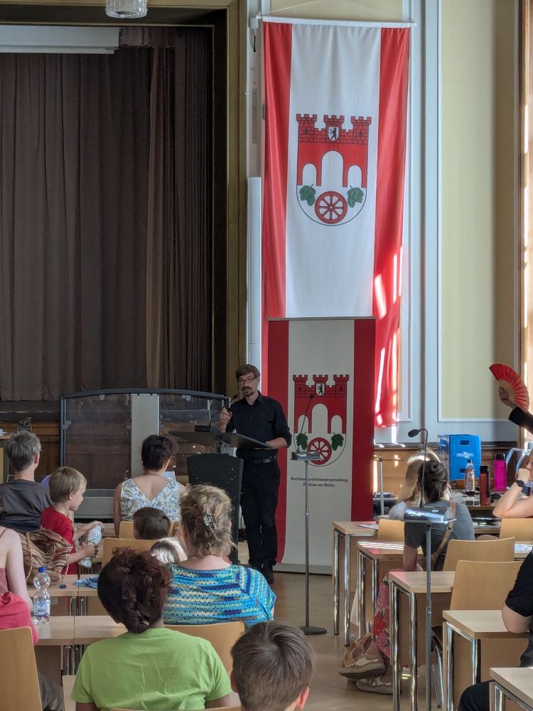 Jurik Stiller, klimapolitischer Sprecher der Linksfraktion Pankow, hält die Laudatio für die Junior-Ranger Pankow vor Publikum im BVV-Saal.