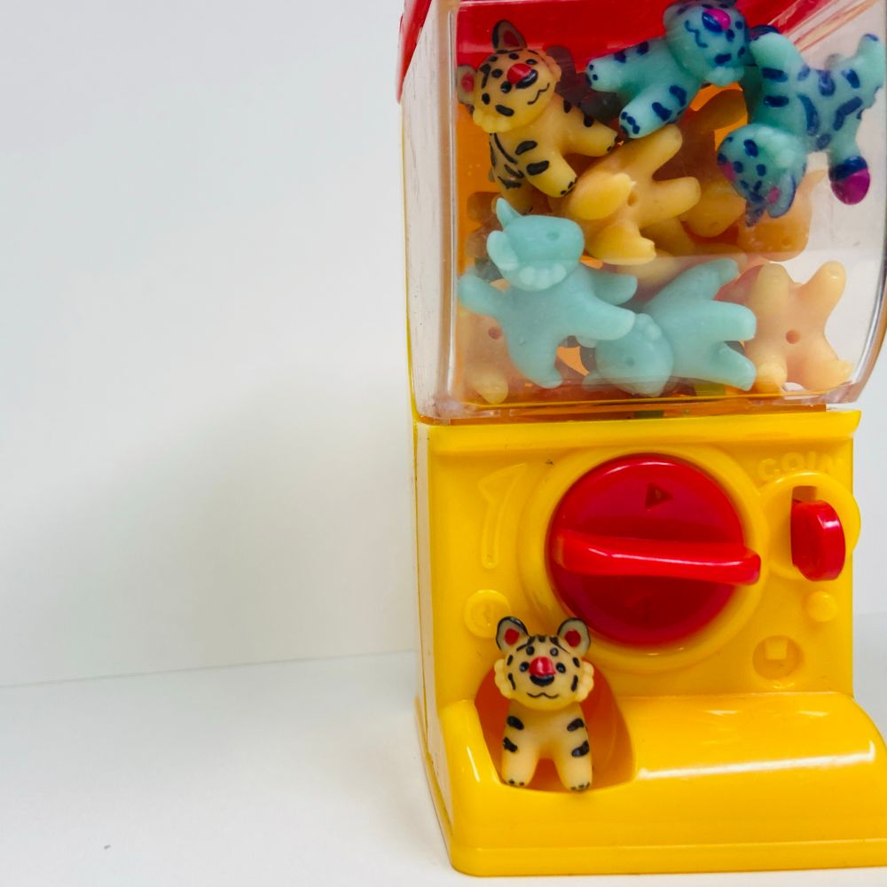 A tiny toy vending machine filled with tiny toy tigers, with one standing in the little prize chute thing at the bottom 