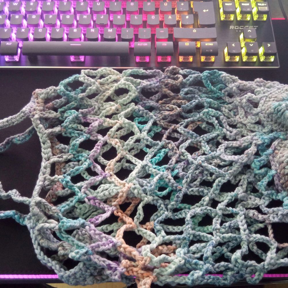 Ein gehäkeltes Obstnetz ausgepackt.
Das Garn ist in verschiedenen Blau und Lila Tönen.