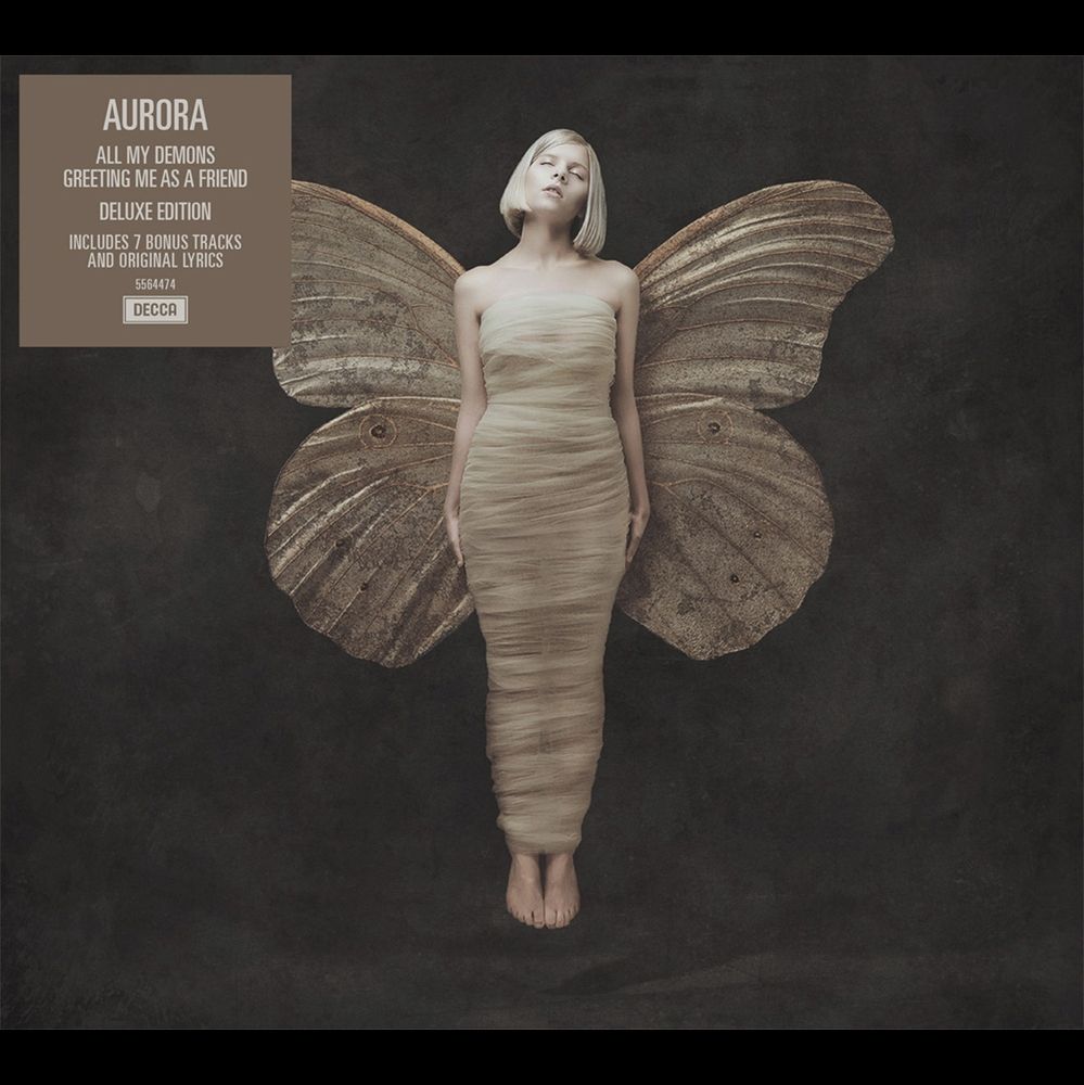 The album cover for All My Demons Greeting Me as a Friend by Aurora. It features Aurora with a platinum blond, short haircut, floating in the air wrapped in silk with moth wings behind her.