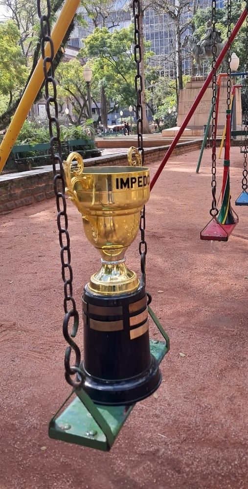 Taça da Impedcopa em um balanço infantil numa praça. Dia de sol. 
