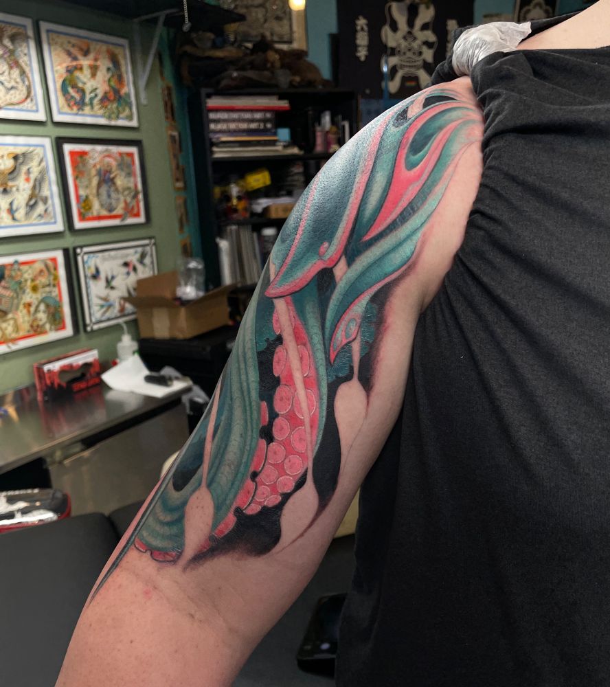 A teal and pink tattoo with tenticles and organic shapes covering the whole upper arm