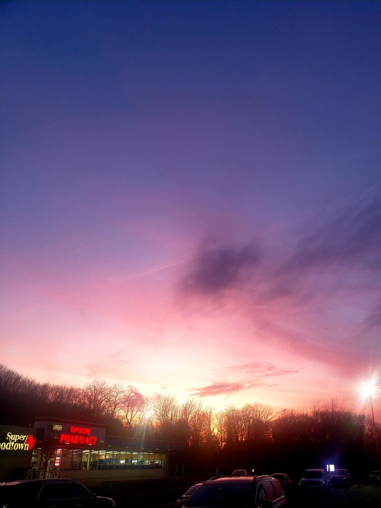 A sunset in a grocery store parking lot. The sky fades from navy, to purple, to pink, to yellow above a New Jersey pharmacy. The smell of cooking ham permeates the air. There's a dog, too. Pretty dope.