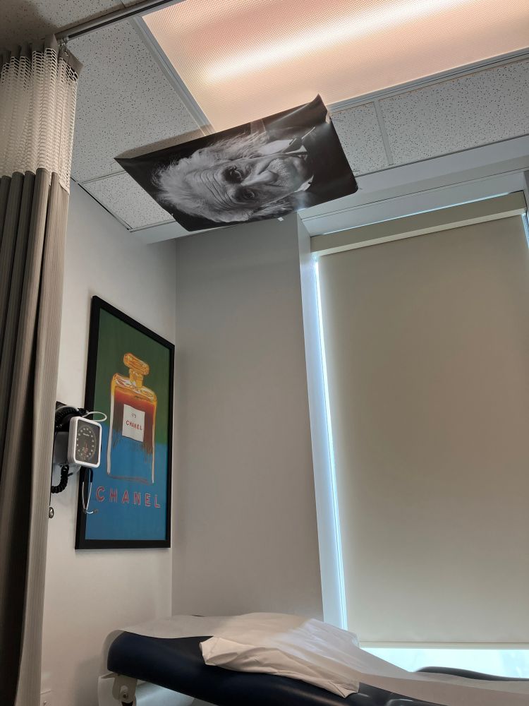 Exam table at gynaecologist’s with a poster for Chanel No. 5 on the wall, and a portrait of Albert Einstein on the ceiling 