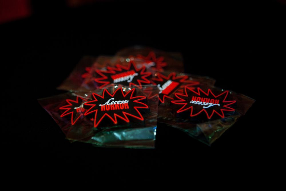 A handful of black, red, and white spiky logo Access:Horror magnets on a dark table.