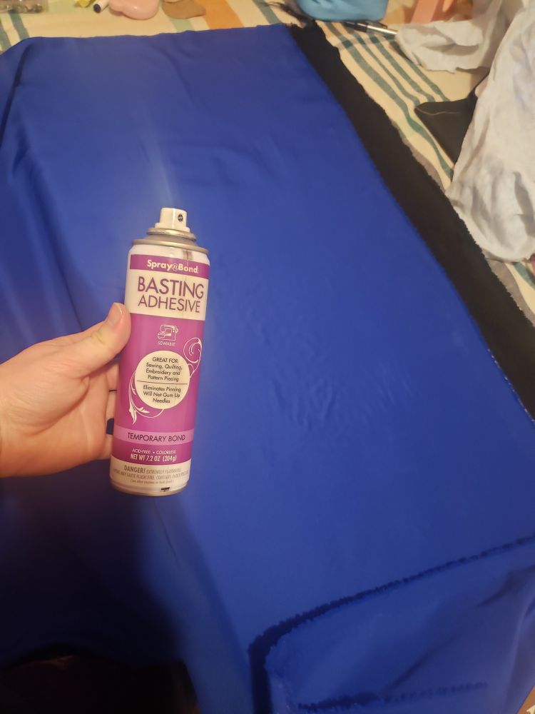 Blue fabric on top of black fabric with a can of Spray Bond Basting Adhesive held up in view