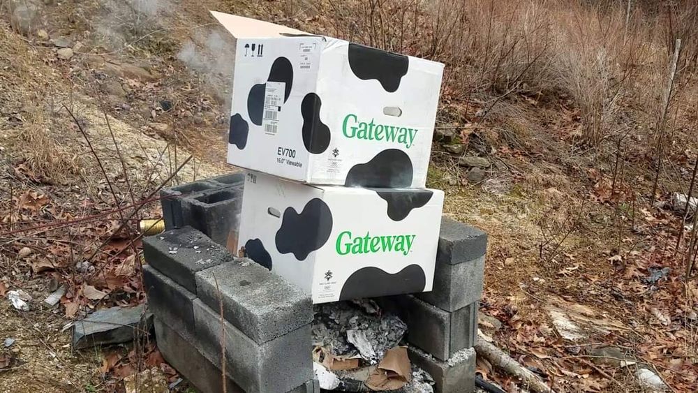 pile of burning cowprinted gateway boxes in a forest during fall in some kind of cinderblock fire pit. One of my all-time favorite images. Credit: wikicommons for some reason?! probs could reverse image search for context but I like the mystique