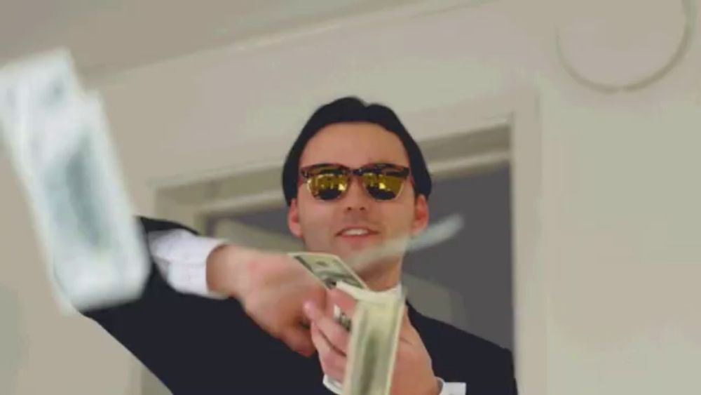 a man in a suit and sunglasses is holding a bunch of money in his hand .