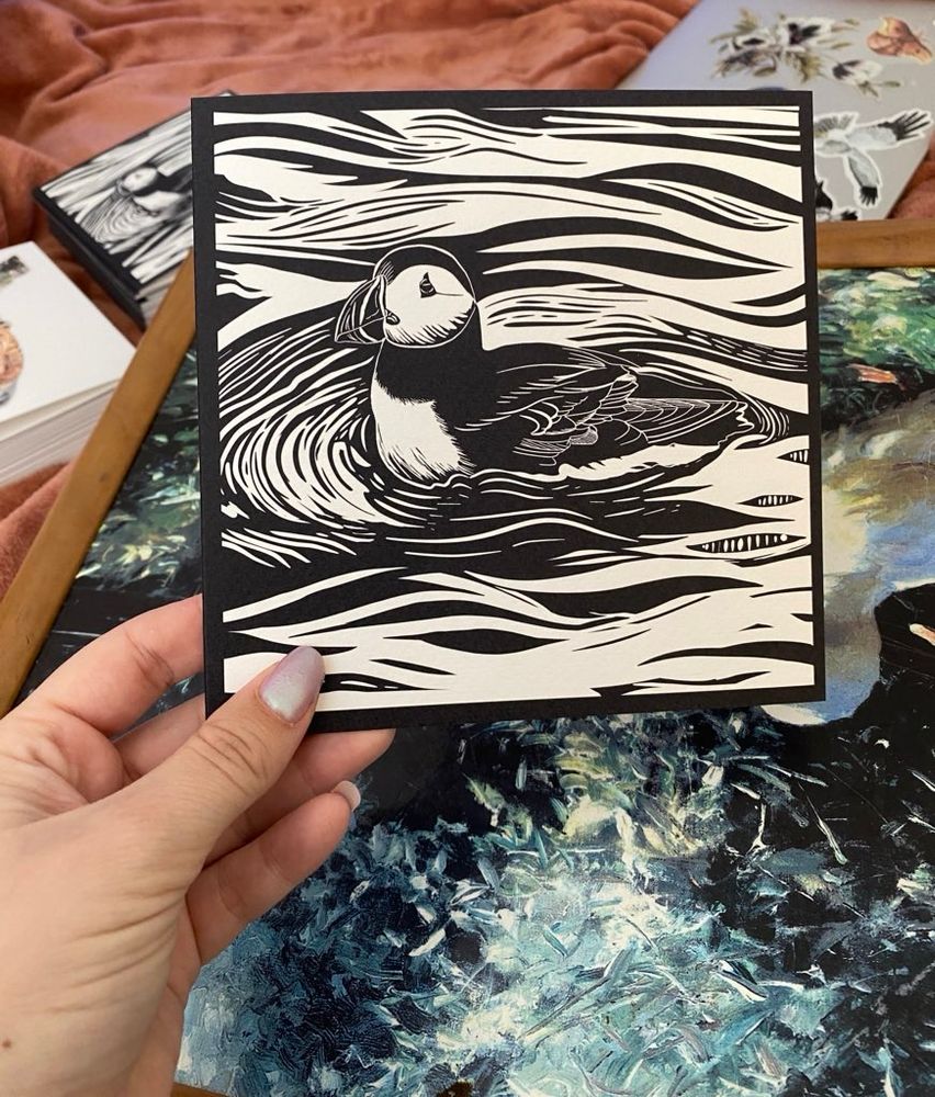 My black and white digital drawing in a linocut style of a puffin being held up 