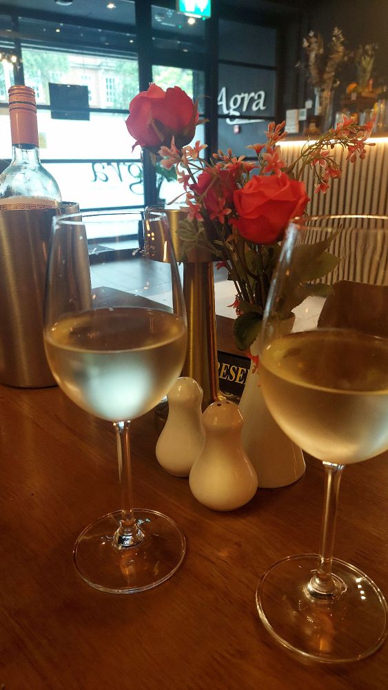 Two glasses of wine. Pink roses in a small vase in background. 