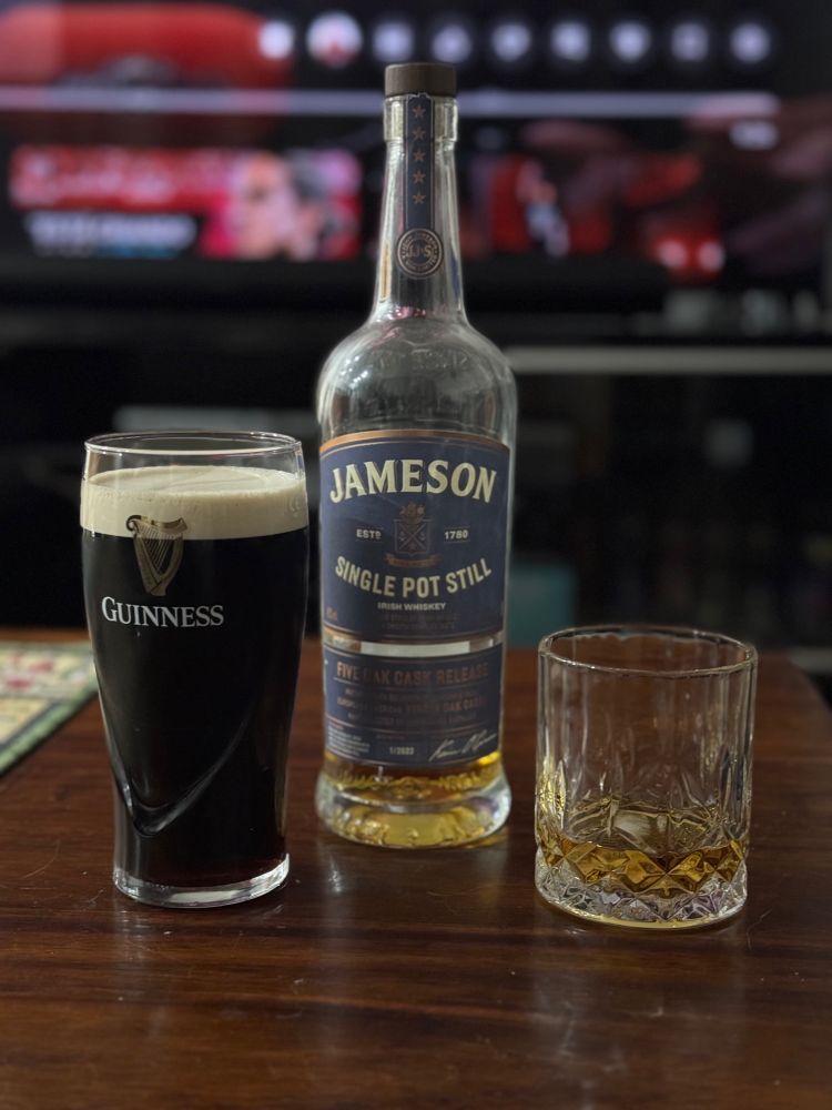 On a coffee table sits a pint of Guiness and a tumbler of whiskey next to a bottle of Jameson Single Pot Still Whiskey