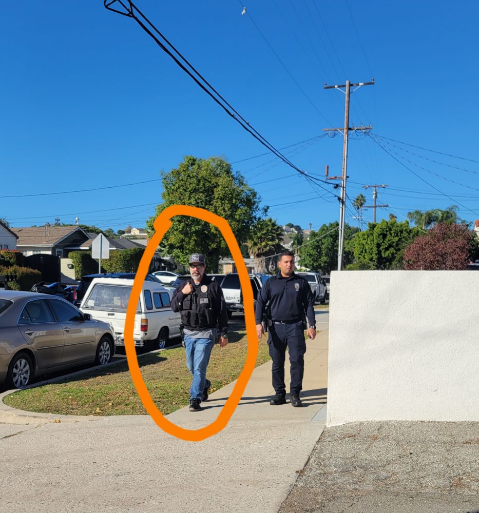Police officers walking towards the camera. The one on the left is the one who looks like Neegan from The Walking Dead tv show. Fun alt text fact, he did not like being called that