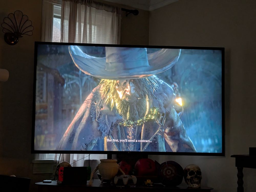 A photo of the opening cinematic of Bloodborne. A decrepit, bearded man leans forward and says, "But first, you'll need a contract..."