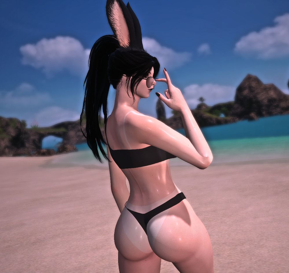 Lucy on her private beach looking backwards, with her right arm up and right hand adjusting her sunglasses.