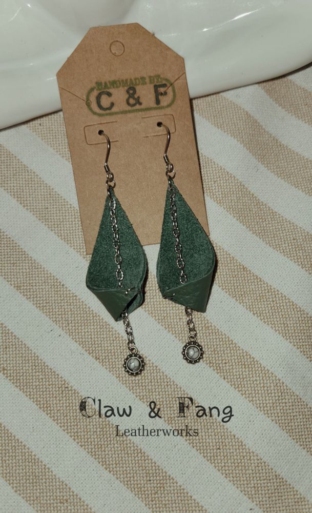Photo of a pair of green leather earrings with white agate stone charms hanging down the center from a delicate silver chain. These were handmade by Claw & Fang.