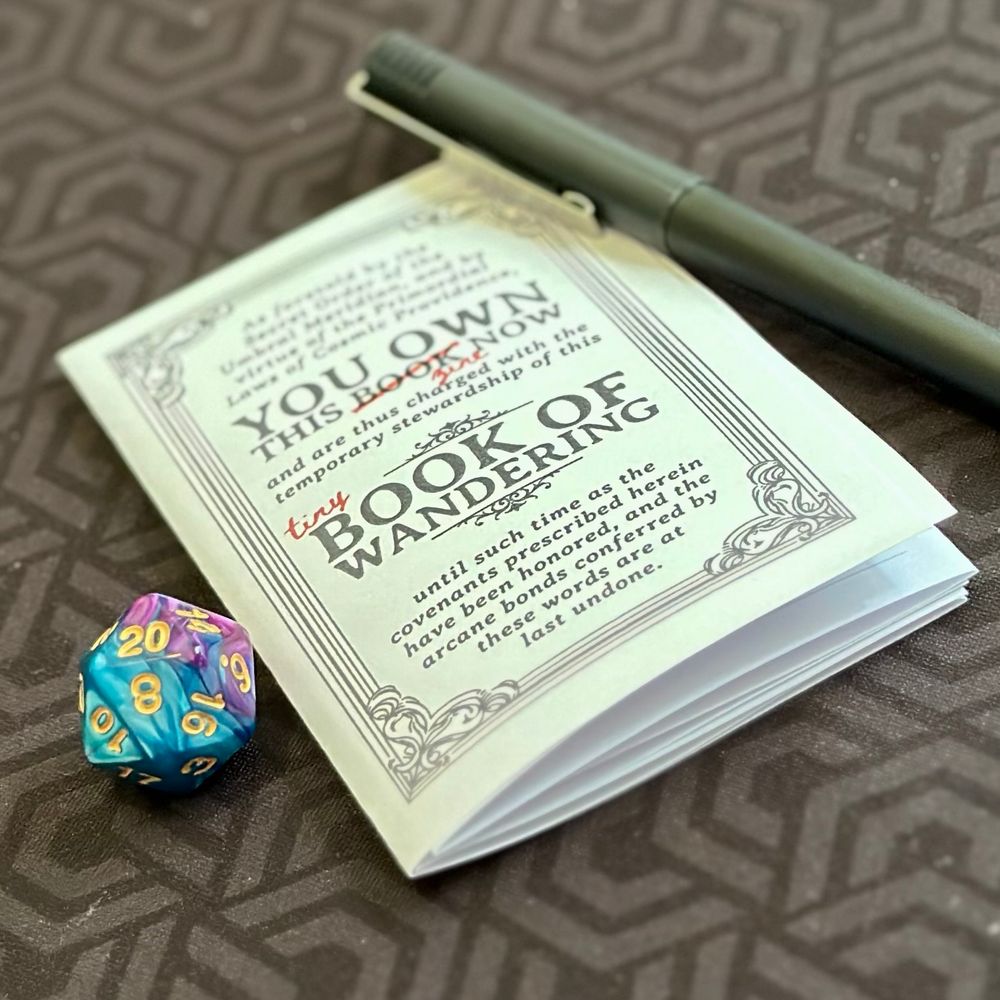 A folded zone-style Tiny Book of Wandering with a D20 on one side and a pen on the other. 