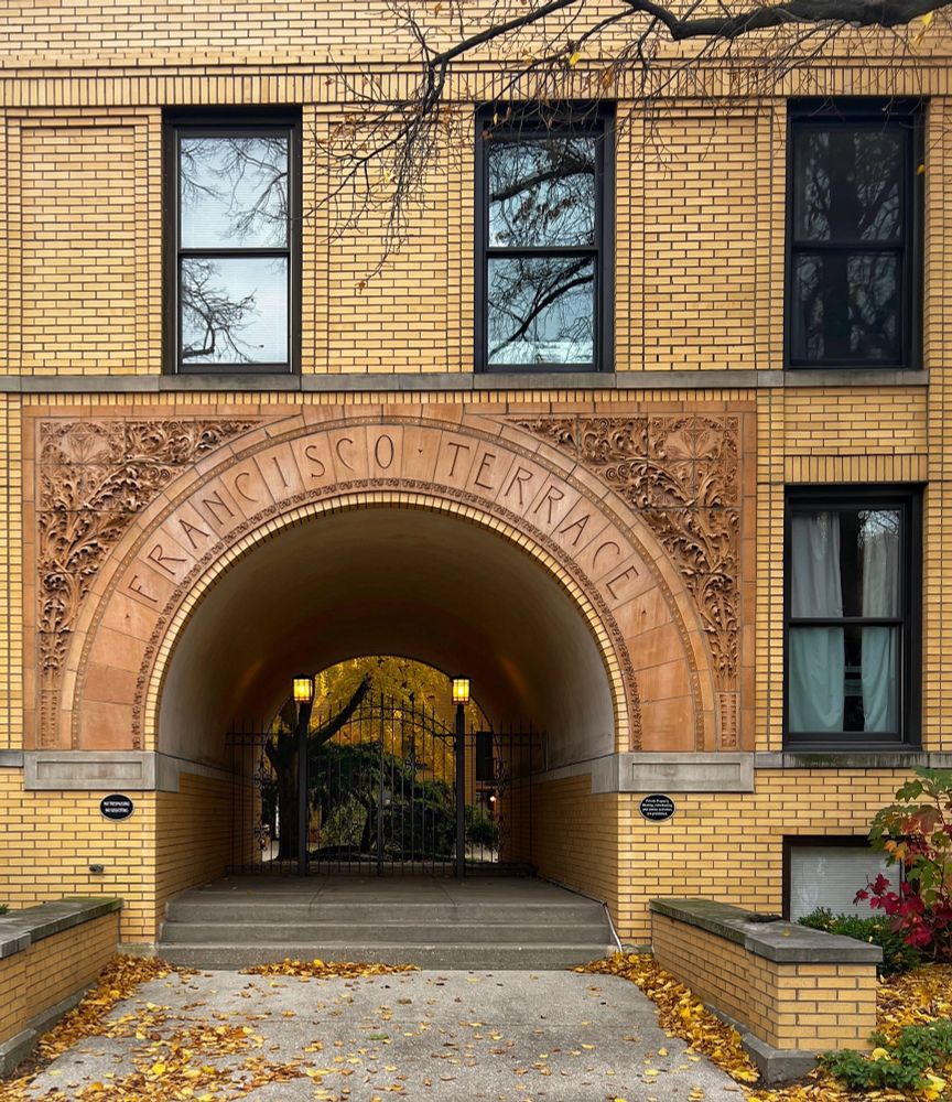 Ornate stone arch designed by Frank Lloyd Wright opening to a gated passage with bright autumn trees visible beyond. 
Oak Park, Illinois 
