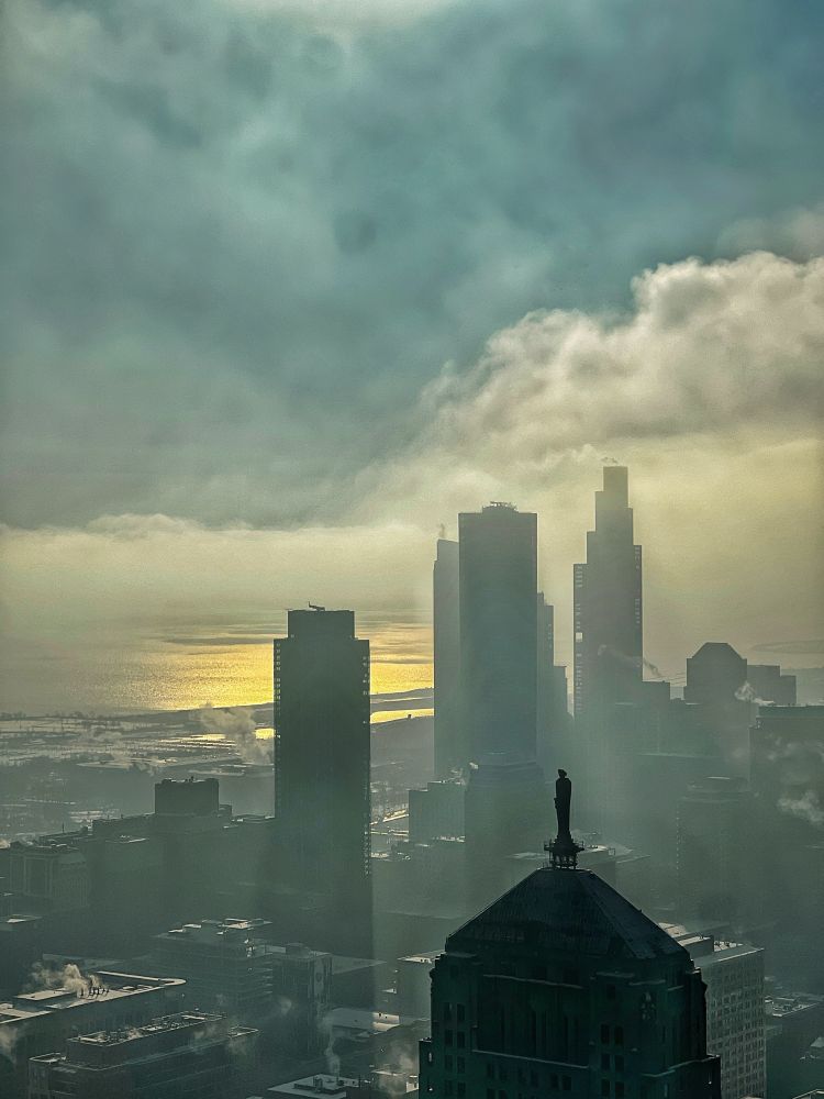 View southeast from downtown Chicago at 9:00 AM on a December morning showing the Chicago Board of Trade building with its rooftop statue in the foreground, a row of skyscrapers fading into mist, and Lake Michigan glowing