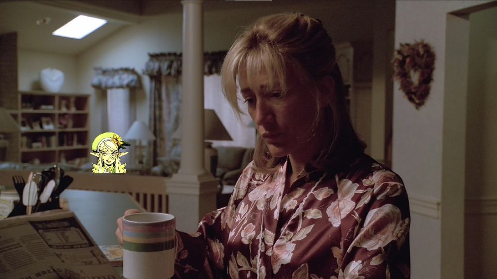 Edie Falco drinking coffee in a kitchen. 