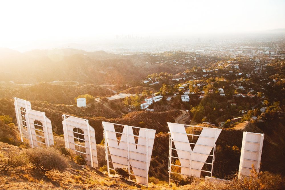View from behind the iconic Hollywood sign in Los Angeles, California, overlooking the city and surrounding hills during a golden sunset.