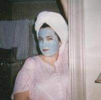 Woman with a towel on her head and a blue cleansing mask on her face.