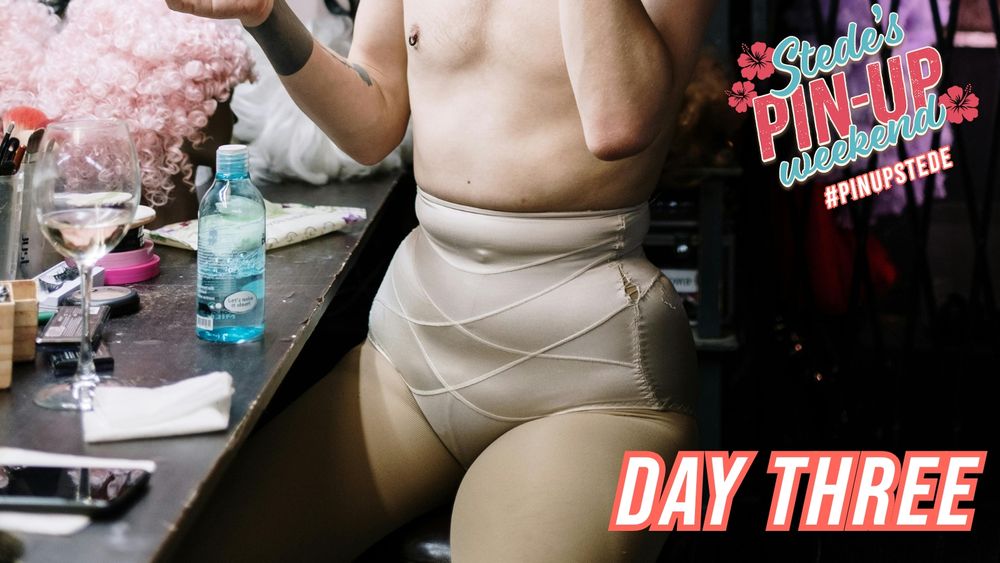 A graphic for day three of Stede's Pin-up Weekend event hosted by @bottomstedeweek. A person sits in front of a worn vanity, surrounded by cosmetics and beauty accessories. They are in nude tights and wearing matching satiny shapewear. They are bare chested with tattoos on their arms and a dark metallic nipple piercing. The event logo is in the top right of the image and the words 'days three" are in the bottom right.